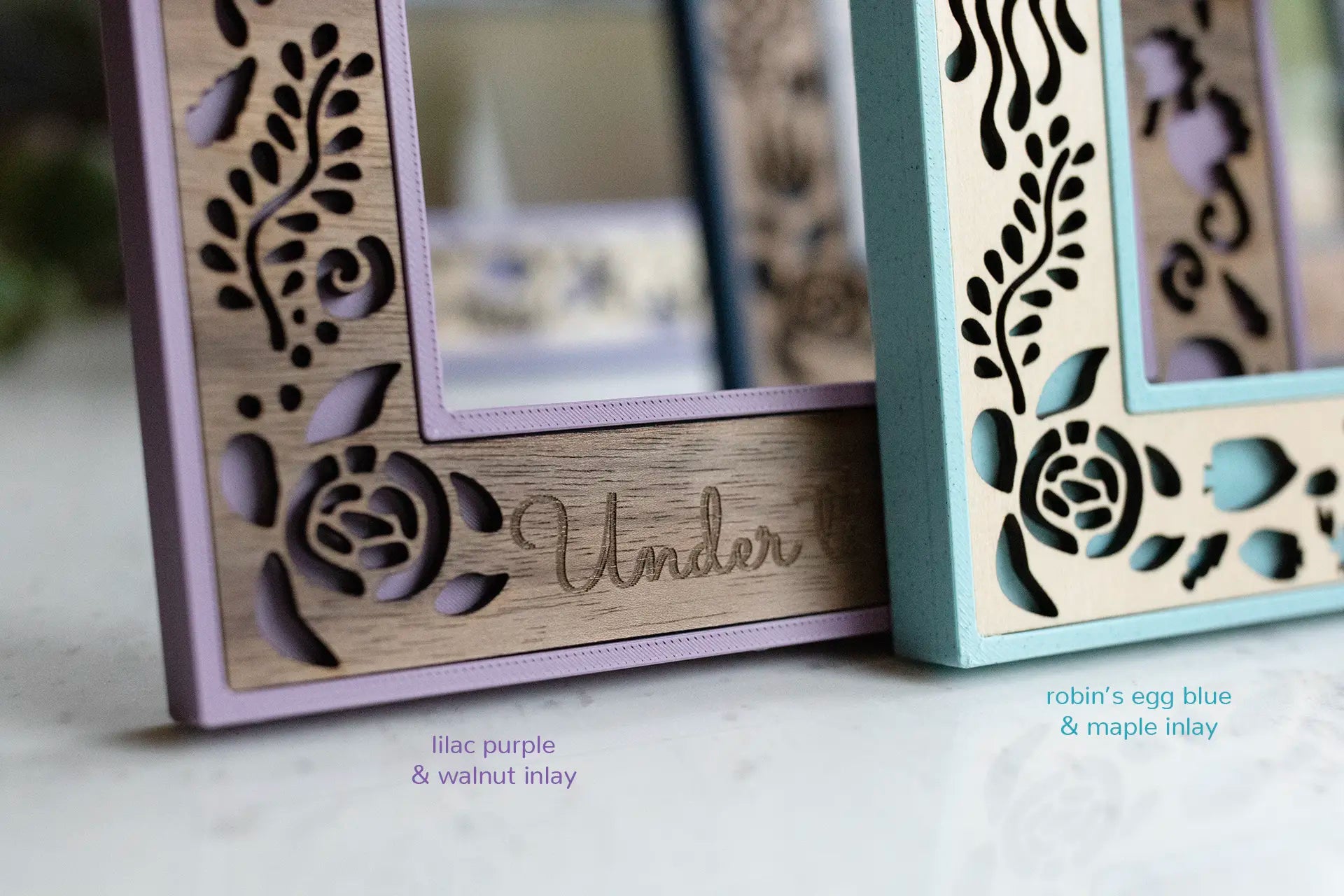 Detail view of two laser cut sea creature picture frames showing walnut and a purple border on one and maple wood and a blue border on the other. Shows variation in wood grain and coloring from frame to frame.