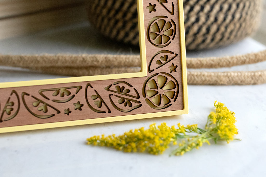 Laser engraved lemon picture frame with cute lemon slices and lemon wedge designs. There is a yellow flower lying in the foreground.