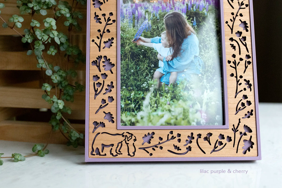 Cherry wood picture frame with lilac purple housing and laser-cut woodland cutouts with a mama bear snuggling a baby bear. The frame displays a photo of a mother holding her child in a field of flowers.