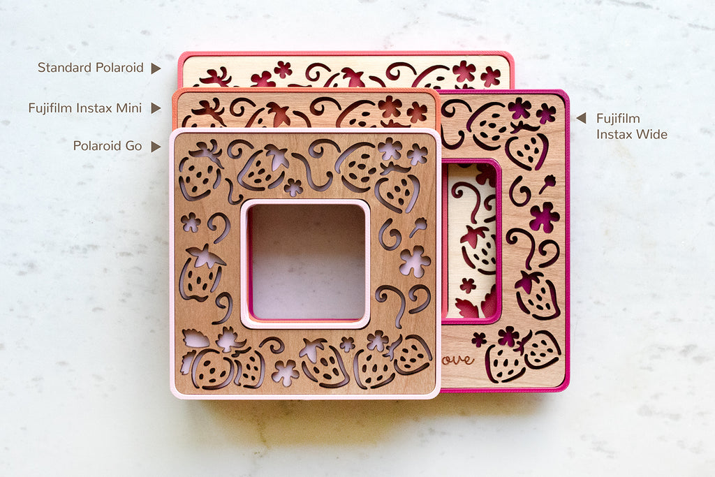Four polaroid frames with strawberry laser cut design stacked on top of each other. The frames are a variety of pink and red colors. Sizes include Standard Polaroid on the bottom, followed by Fujifilm Instax Wide, Fujifilm Instax Mini, and Polaroid Go on the top of the stack.