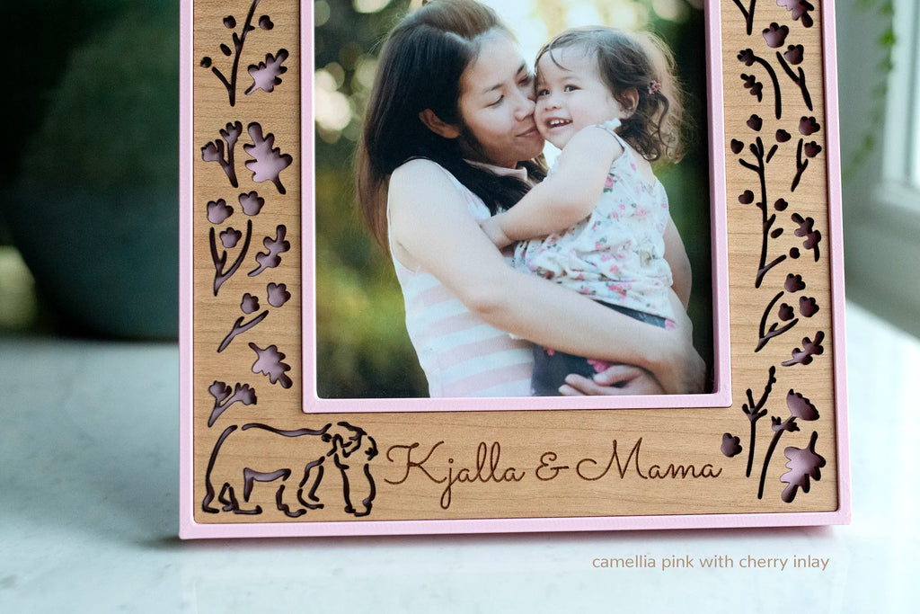 Close up of a floral wood frame featuring mama and baby bear hugging, displaying a photo of a mom hugging her daughter. The frame is camellia pink with a laser-cut cherry wooden inlay.