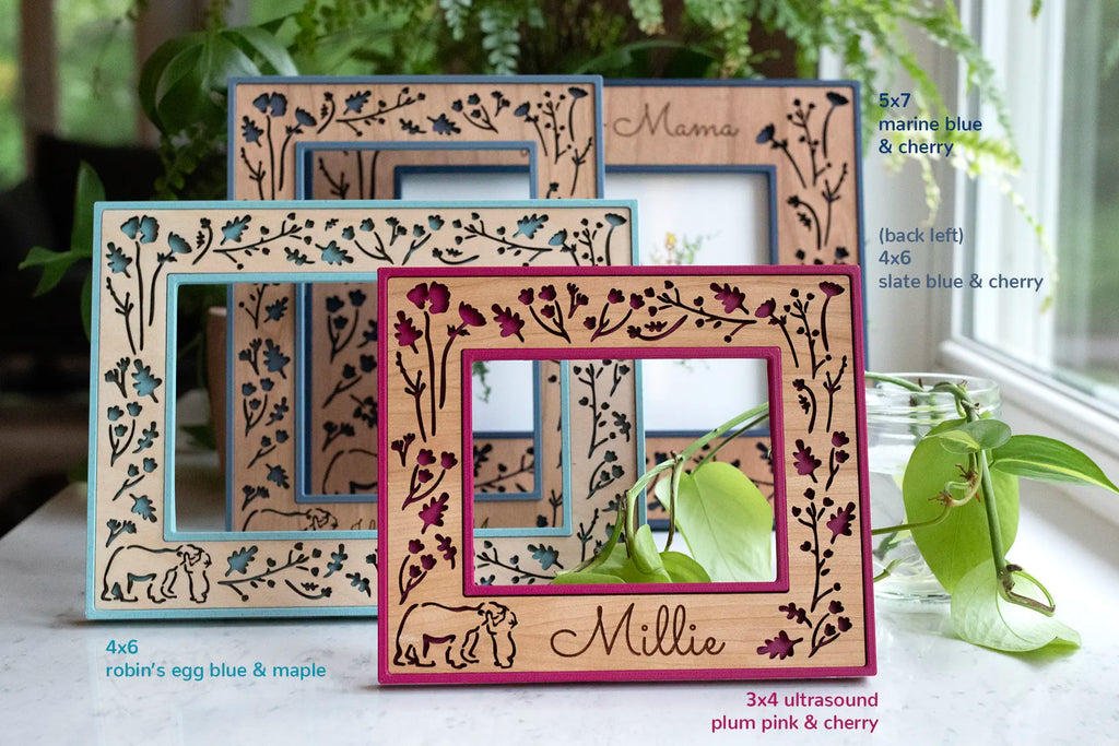 A mama and baby bear custom picture frame in an assortment of sizes, colors, and wood types. The designs are bright and playful. The wooden border of the frame features intricate laser cut woodland flowers and leaves with a baby bear hugging mama bear in the bottom left-hand corner.