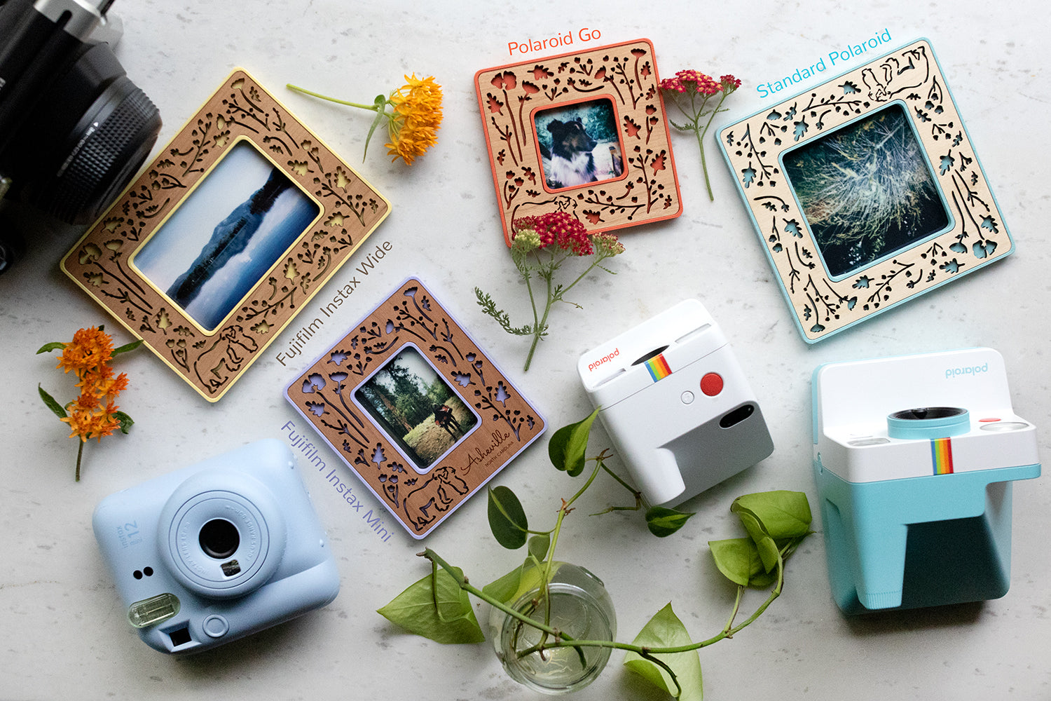 An assortment of colorful Polaroid photo frames including Instax Mini, Polaroid Go, Standard Polaroid, and Instax Wide. The frames are lying next to several different types of Polaroid and Fujifilm cameras that are used to take the photos.