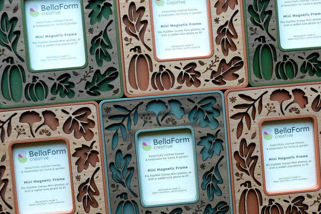 Overhead view of fall leaves magnetic frames in moss green, sage green, and terracotta arranged in a pattern, each with laser-cut autumn leaf and pumpkin cutouts and a BellaForm Creative insert card noting the Instax Mini and wallet-size photo fit.