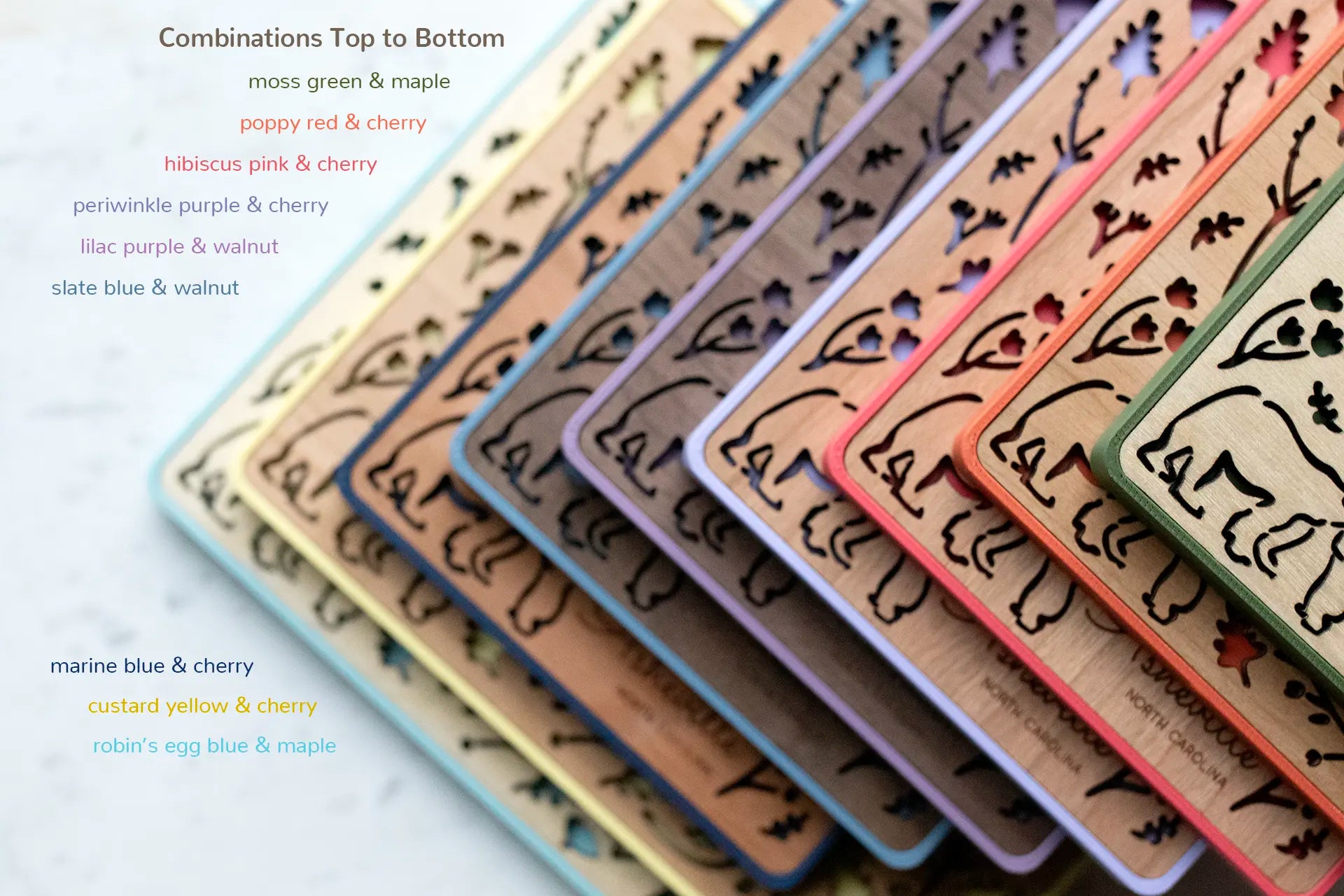 An assortment of nine magnetic mama bear and baby bear frames with various wooden inlay types. Colors include: moss green, poppy red, hibiscus pink, periwinkle purple, lilac purple, slate blue, marine blue, custard yellow, robin's egg blue. The frames are displayed in a stack with only the corners showing to reveal the colors.