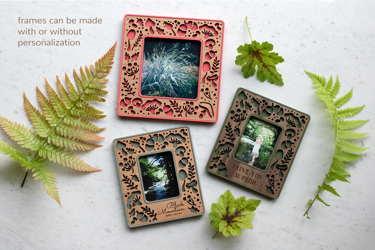An assortment of three mini mushroom frames with laser cut wooden inlays. The image reads "frames can be made with or without personalization." Frames are magnetic and lightweight to hang on the refrigerator, making great mushroom kitchen decor. The frames are surrounded by fern fronds and other greenery.