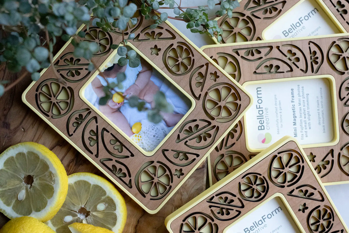 An assortment of hand crafted lemon frames with magnets for the refrigerator. These instax mini frames are yellow with a cherry wood laser-cut inlay. They are pictured next to lemon slices and greenery.