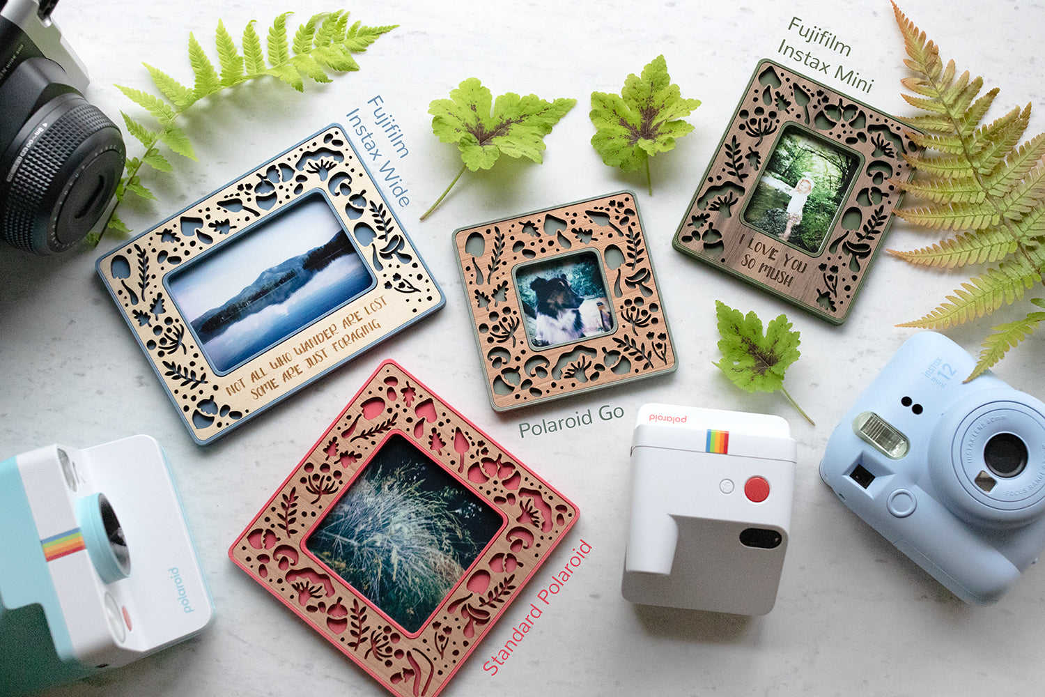 An assortment of magnetic picture frames including various sizes: Instax Mini, Instax Wide, Polaroid Go, and Standard Polaroid. The frames are lying next to several different types of Polaroid and Fujifilm cameras that are used to take the mini photos. The mushroom frame design is shown in four photo sizes in various colors and wood types.