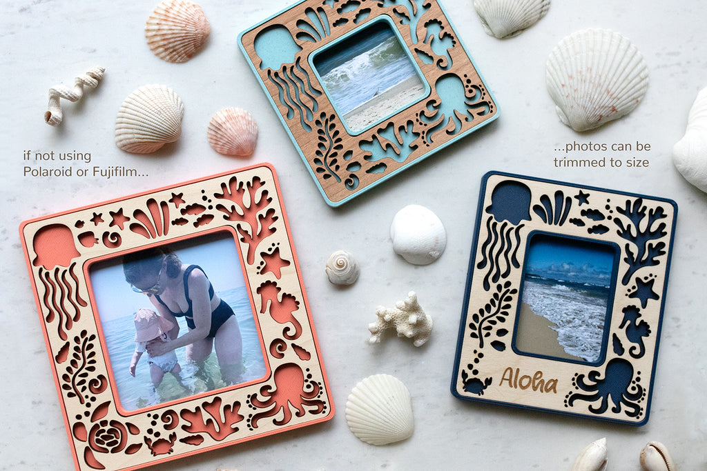 A close-up detail view of three mini magnetic sea creature frames. Frame designs include an octopus, crabs, starfish, jellyfish, sea turtles, fish, and ocean coral. The frames are pink coral, light blue, and navy with various wooden inlays. Mini frames display photos of the ocean and people swimming in the ocean.