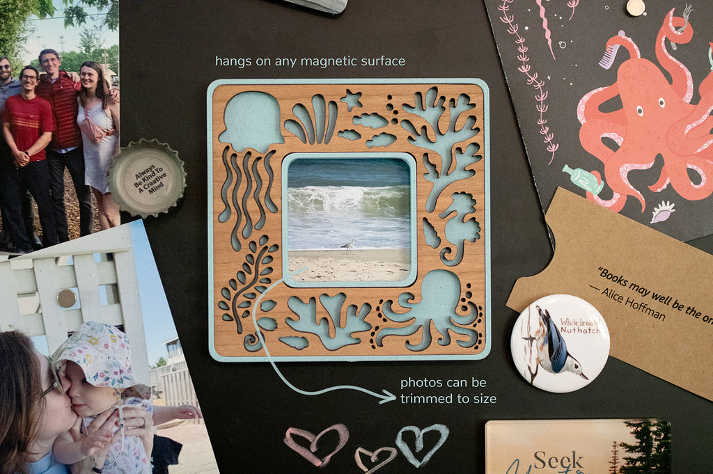 A small polaroid go magnetic frame with sea creature design. The wooden border is laser cut using cherry wood. There is a note that reads "frame hangs on any magnetic surface" and "photos can be trimmed to size". This frame displays a tiny trimmed beach photo.