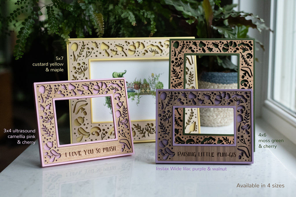 Four whimsical mushroom photo frames with various colors and wood types. Frames are yellow with maple, green with cherry, purple with walnut, and pink with cherry. Sizes include 5x7 frame, 4x6 frame, 3x4 ultrasound frame, and Instax Wide frame.
