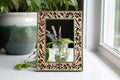 A green laser cut mushroom picture frame with intricate cherry wood inlay. The frame has a whimsical aesthetic and is surrounded by greenery and flowers. 4x6 picture frame with jar of flowers visible through the frame.