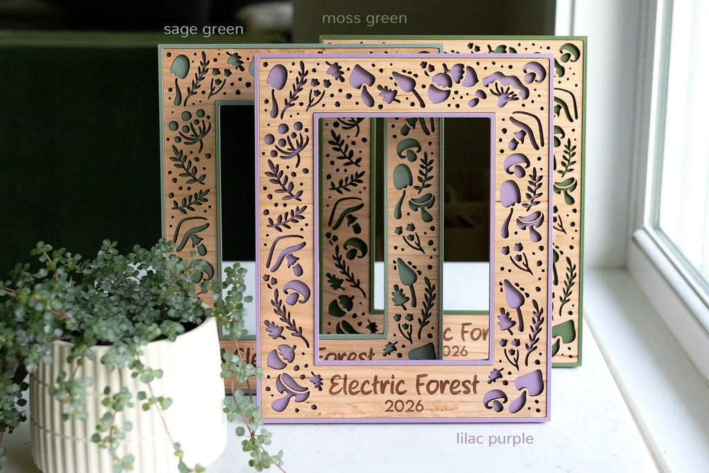 Three personalized mushroom picture frames in lilac purple, sage green, and moss green with cherry wood inlay, engraved with a custom festival name and year as a music festival keepsake, shown reading “Electric Forest 2026.”