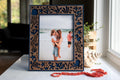 Front view of a walnut picture frame with navy blue housing and laser-cut ocean cutouts of an octopus, jellyfish, seahorse, starfish, coral, and seashells, holding a beach family photo.