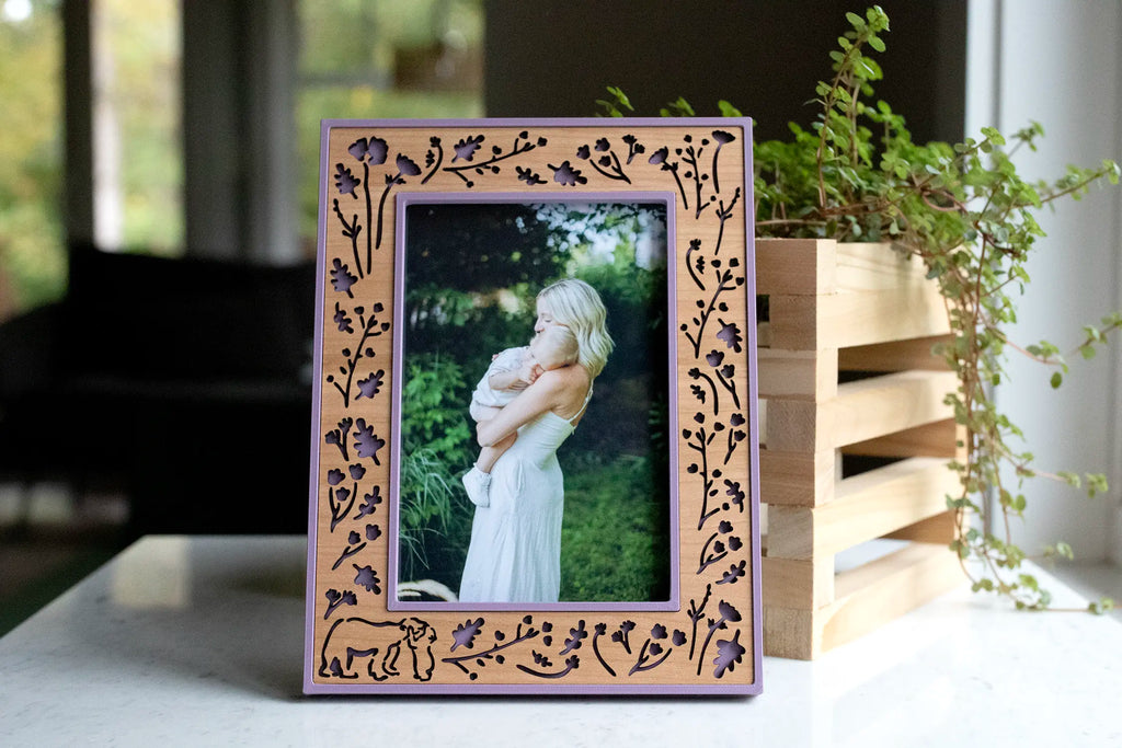 Front view of a cherry wood picture frame with lilac purple housing and laser-cut wildflowers, branches, and bear cutouts, holding a mother-and-baby photo.