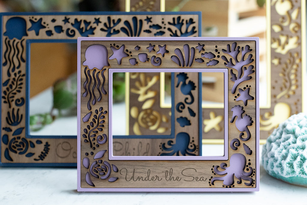 Personalized laser engraved photo frames. Front frame includes a laser engraved message that reads "Under the Sea." Back frame includes a custom message that reads "Ocean Child." Customers can request customization with their laser cut frame designs.