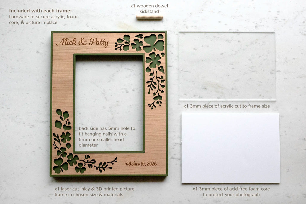 Components included with each Irish wedding shamrock picture frame, laid flat: the laser-cut cherry and moss green frame engraved "Mick & Patty, Oct 10 2026," a 3mm acrylic sheet, an acid-free foam core backing, and a wooden dowel kickstand. The back has a 5mm hole for wall hanging.