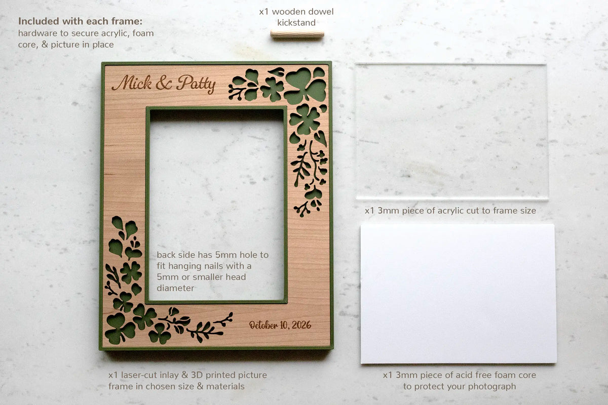 Components included with each Irish wedding shamrock picture frame, laid flat: the laser-cut cherry and moss green frame engraved "Mick & Patty, Oct 10 2026," a 3mm acrylic sheet, an acid-free foam core backing, and a wooden dowel kickstand. The back has a 5mm hole for wall hanging.