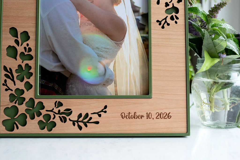 Close-up of laser cut shamrocks and trailing clover in a moss green and cherry wood inlay frame. Displaying an engraving of the wedding date "October 10, 2026".