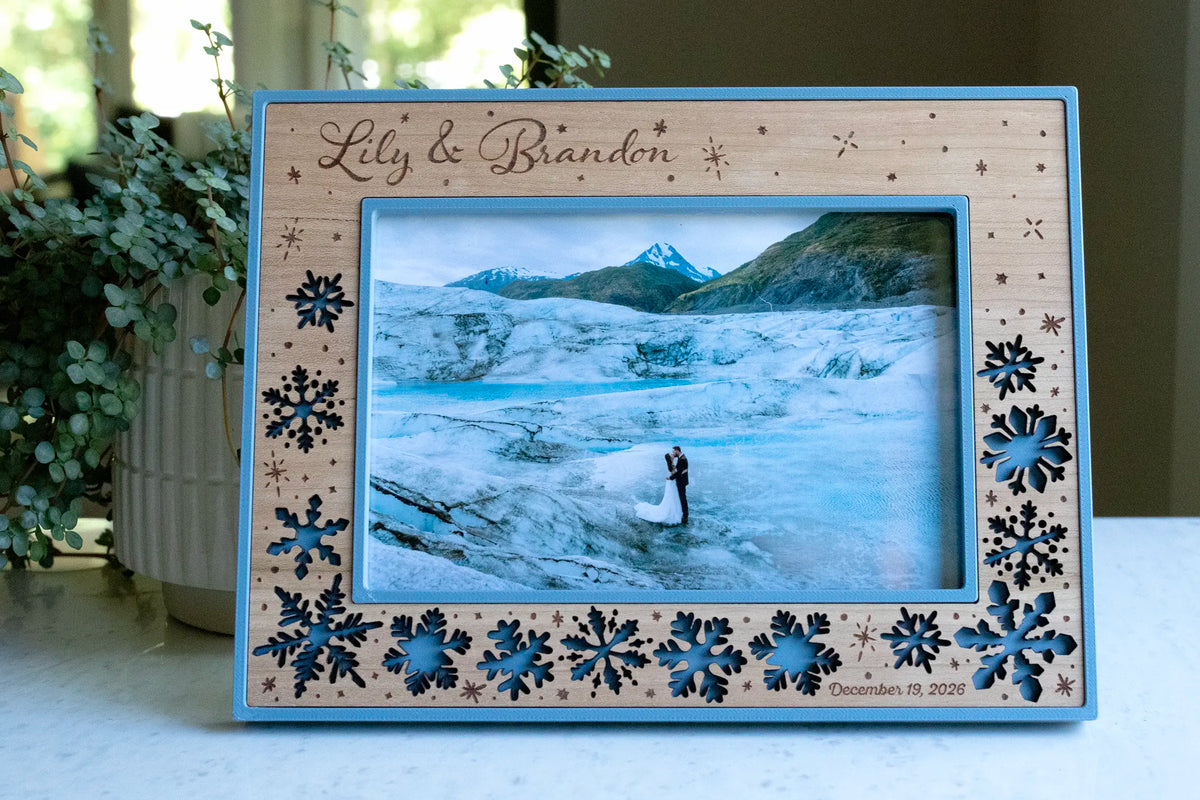 A personalized, laser-cut winter wedding picture frame with falling snowflakes in a wood inlay. This 4x6 personalized picture frame features the newlyweds names engraved in the top left corner and their wedding date engraved in bottom right.