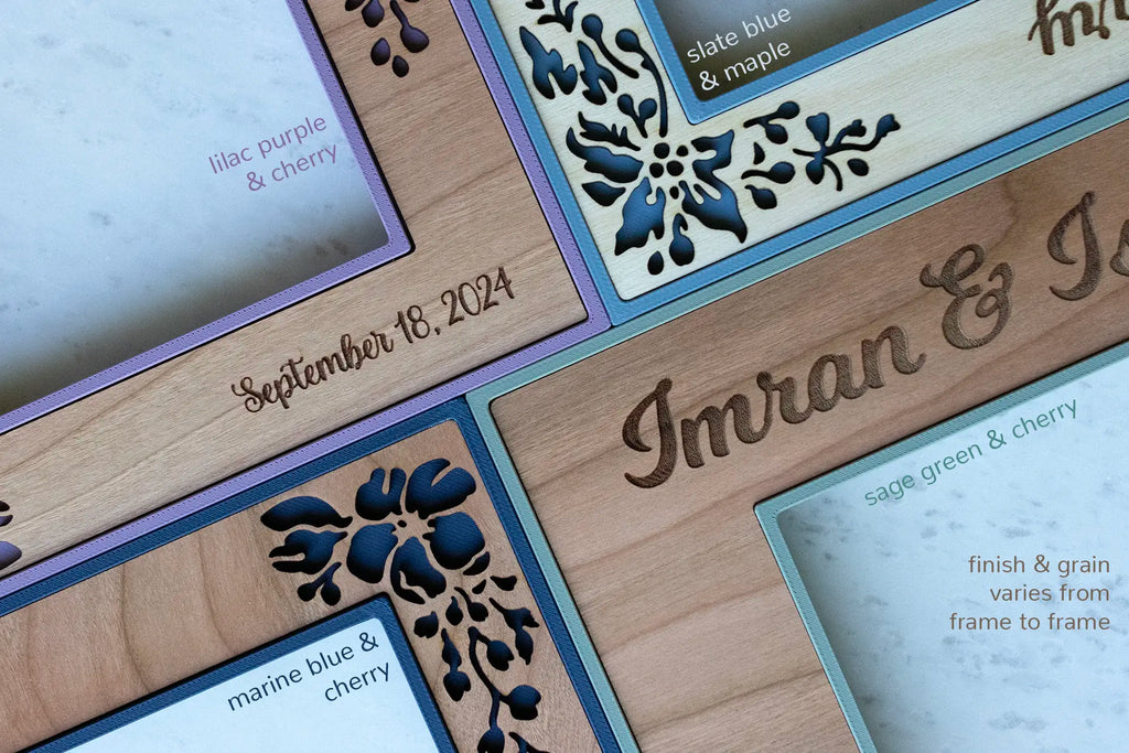 A close-up detail view of various wood grains and personalized engravings on four wedding picture frames. The frames displayed have flowers cut out of the cherry and birch. The frame borders are colorful in sage green, lilac purple, and various shades of blue.