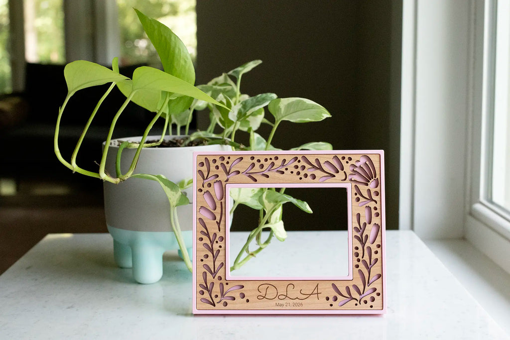 A personalized pink floral picture frame for a new mom keepsake gift. The frame holds a baby's sonogram photo. Picture frame can be personalized with a child's name and date of ultrasound photo or birth date. Frame features a custom laser cut floral design with personalized engraving details.