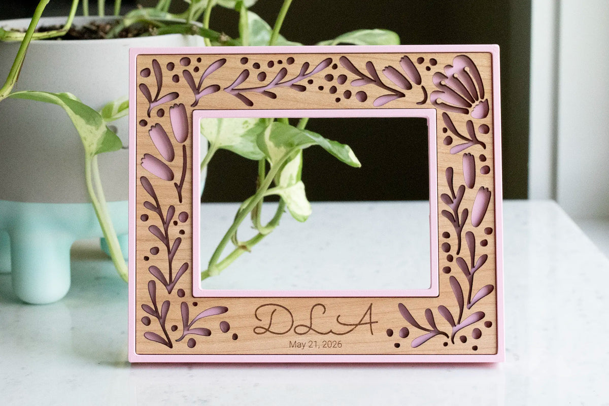 A personalized pink floral picture frame for a new mom keepsake gift. The frame holds a baby's sonogram photo. Picture frame can be personalized with a child's name and date of ultrasound photo or birth date. Frame features a custom laser cut floral design with personalized engraving details.