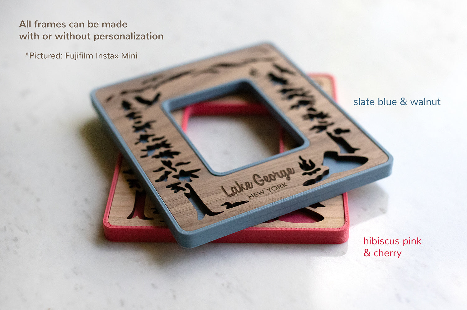 Two Instax Mini magnetic Polaroid photo frames stacked on top of each other and lying on a white counter. The top left corner of the image displays the words: "All frames can be made with or without personalization. Pictured: Fujifilm Instax Mini". The top frame in walnut and slate blue is personalized with the words "Lake George New York."