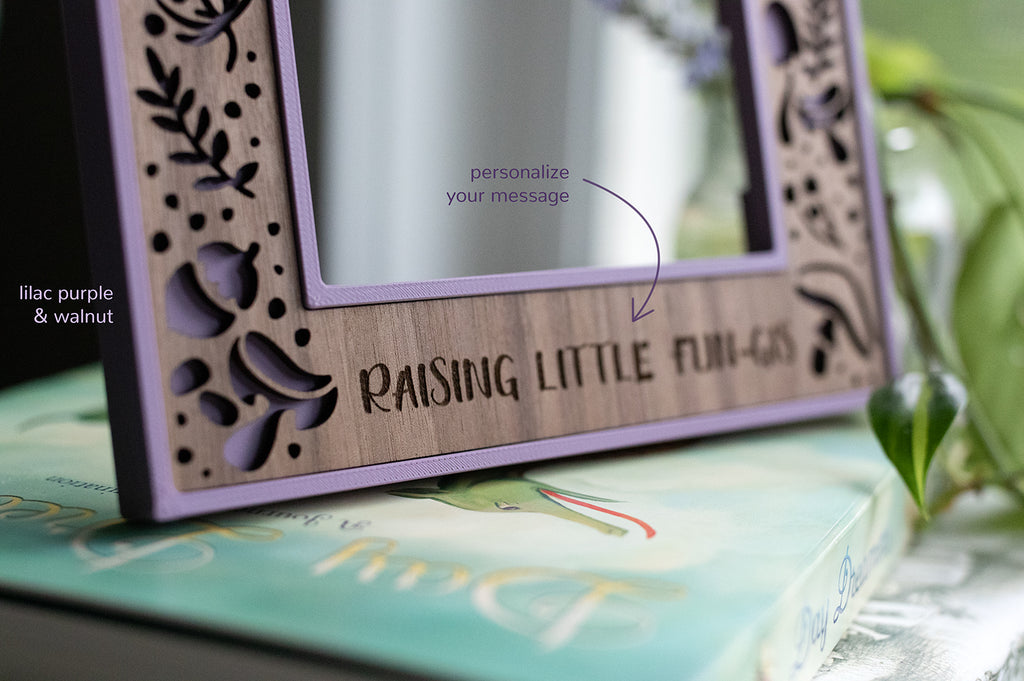 A customizable laser cut picture frame featuring cute mushrooms and acorns. The personalized engraving at the bottom of the frame reads "Raising little fun-gis." There is a note to personalize your message. The picture frame is lilac purple and walnut.