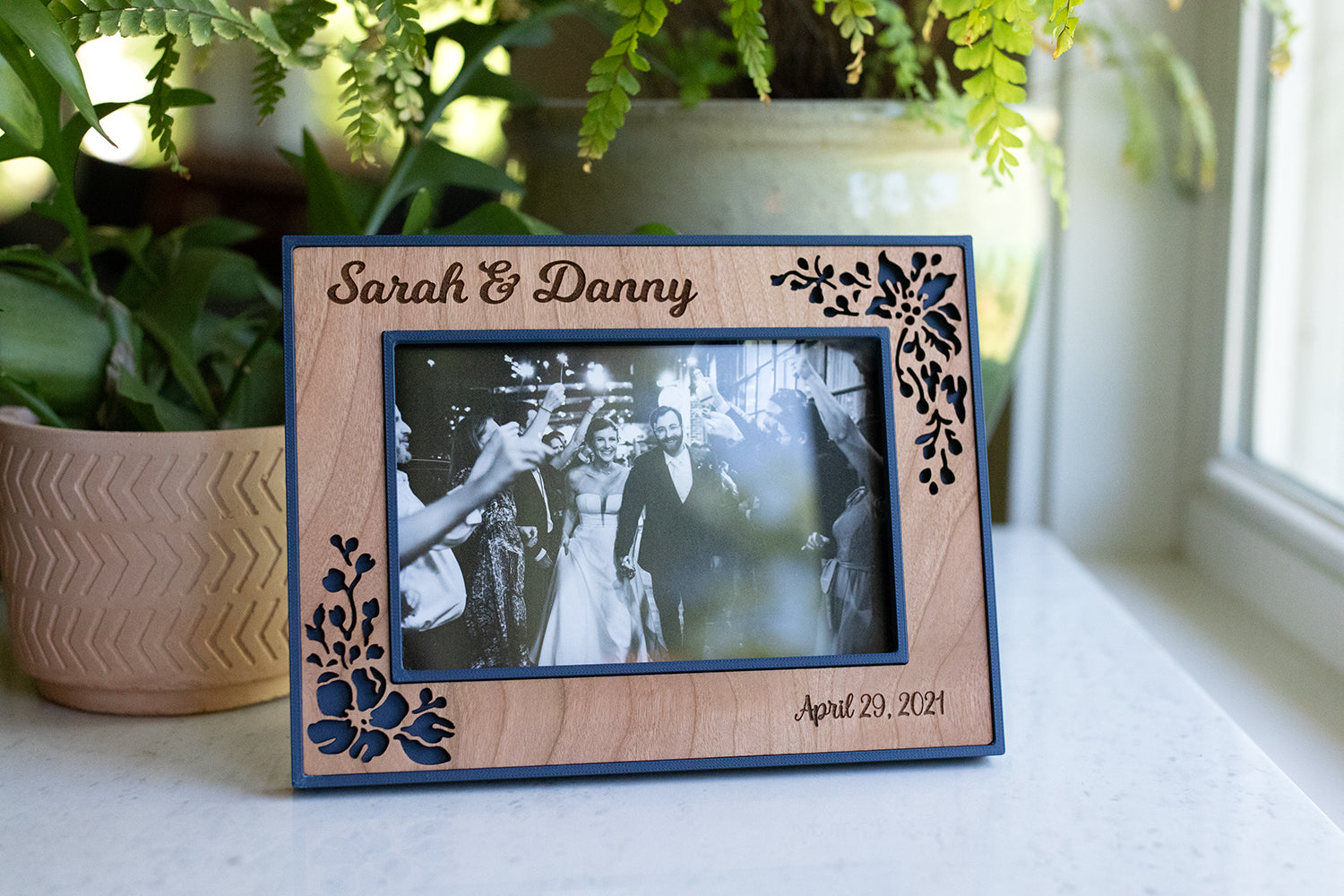 Wedding photo frame in navy blue and cherry wood inlay. The wooden frame inlay has delicate laser cut flowers around the border. The picture frame is 3D printed and laser cut from wood. The frame is displaying a black and white photo of a newlywed couple at their wedding.