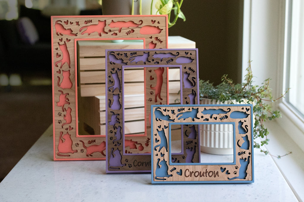 Three custom cat picture frames with cute laser cut cat designs. The cats are playing, running, sleeping, and loafing around. Frames come in a variety of colors and wood types, including walnut, maple, and cherry.