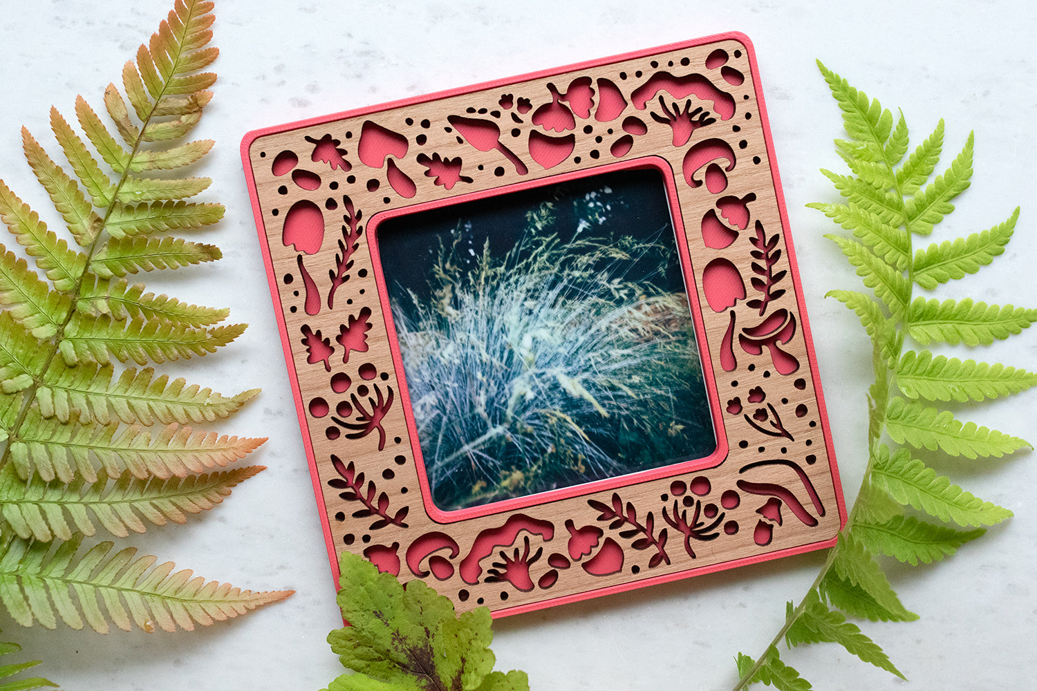 A bright pink magnetic frame with mushroom design. The frame holds a standard size polaroid photo. The frame has a detailed cherry inlay with laser cut mushrooms and acorns. The mushrooms include amanita mushrooms, porcini mushrooms, and other common mushroom types.
