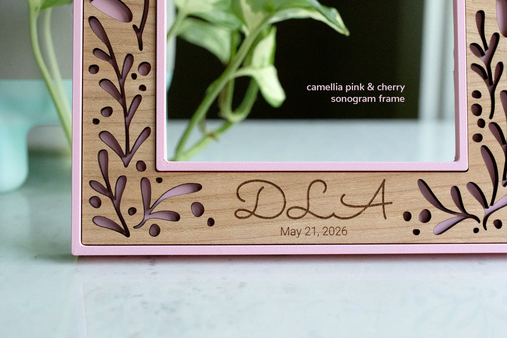 A pink floral ultrasound picture frame for baby and a new mom. This keepsake frame can be engraved with baby's initials, a sonogram date, or a birthday. The frame features a delicate feminine floral design with laser cut wooden inlay.