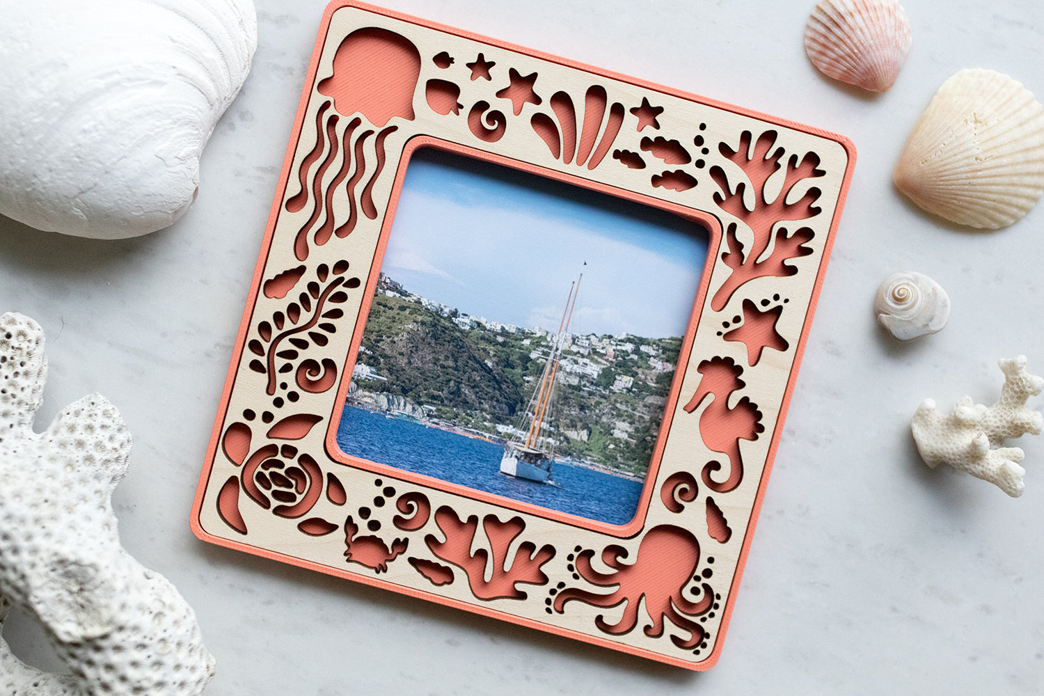 A small magnetic coral beach frame with sea creatures, including an octopus, a sea turtle, jellyfish, starfish, and a crab. The magnetic frame has a laser cut maple inlay and is surrounded by seashells.