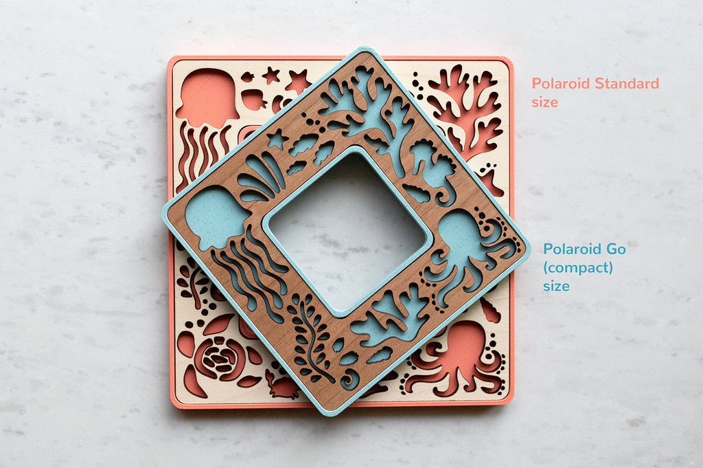 Polaroid picture frames featuring ocean animals. The frames are light blue with cherry wood and coral pink with a maple inlay. The frames hold Polaroid Go and Standard Polaroid photos.