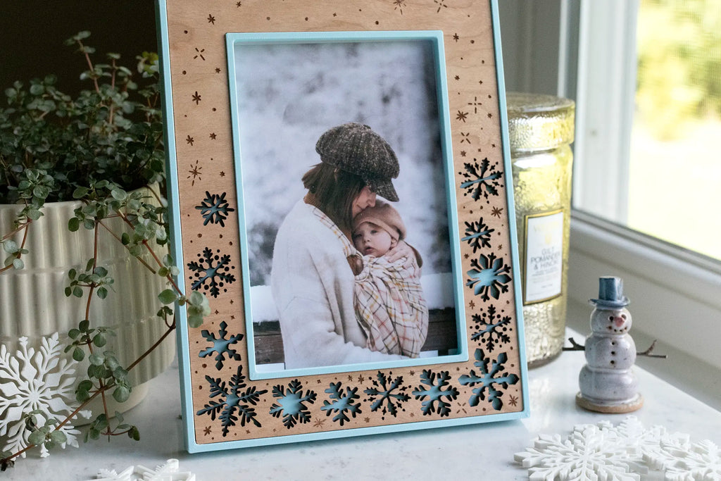 Ice blue snowflake picture frame for holiday photos, available in 4x6, 5x7, and 6x8 frame sizes. This winter keepsake frame features delicate laser-cut snowflakes falling, with a cherry wood inlay and lightweight, durable 3D printed housing.