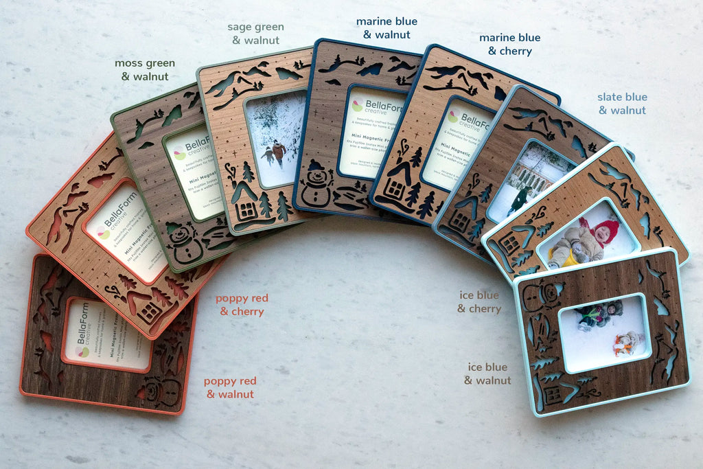 Snowman magnetic frames fanned out showing color and wood options: poppy red, moss green, sage green, marine blue, slate blue, and ice blue, each with walnut or cherry wood inlays.
