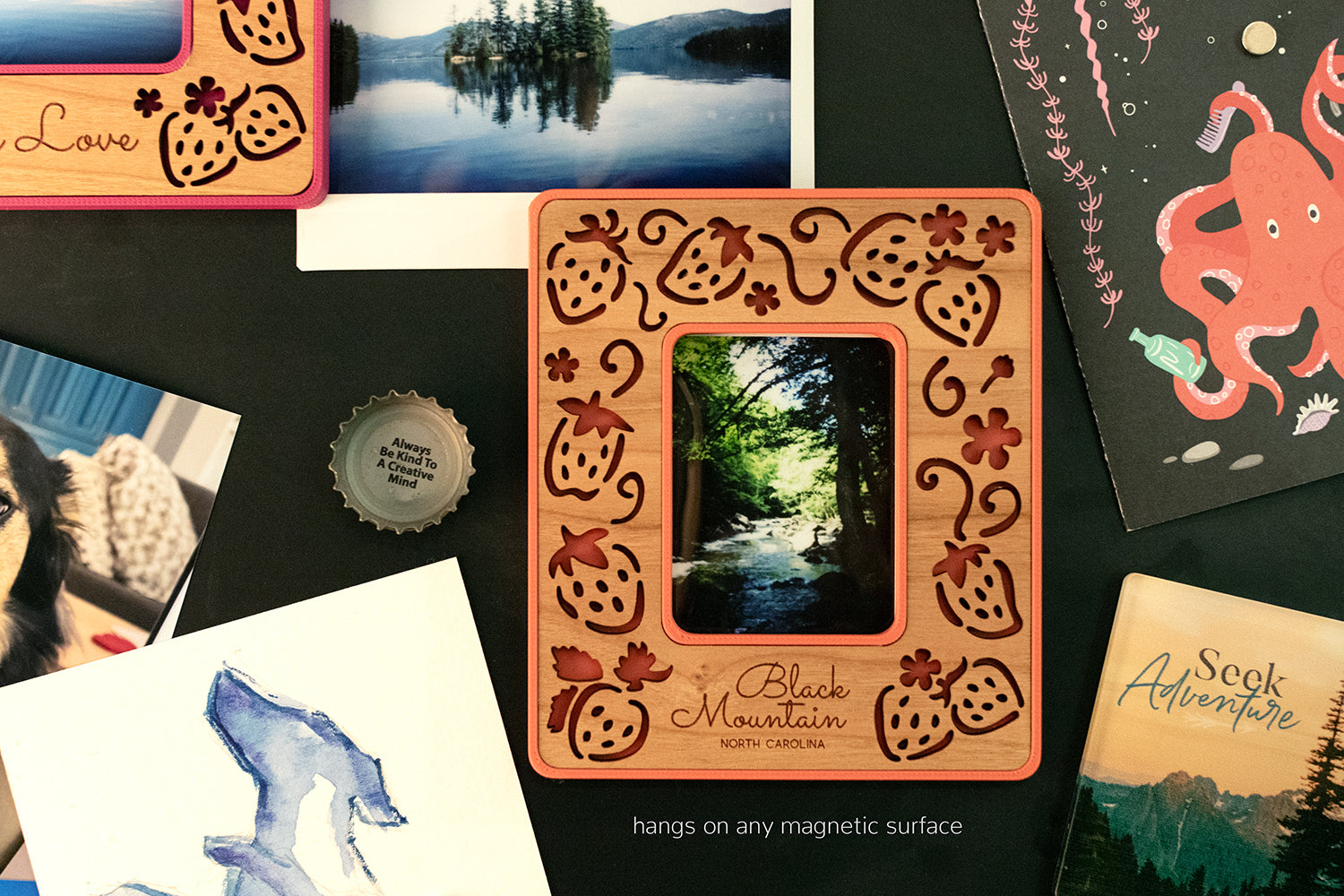 A close-up detail view of a laser engraved Polaroid photo frame for Instax Mini hanging on a black, magnetic chalkboard. The frame has a cherry wood inlay and a red border and includes the customized message: "Black Mountain North Carolina".