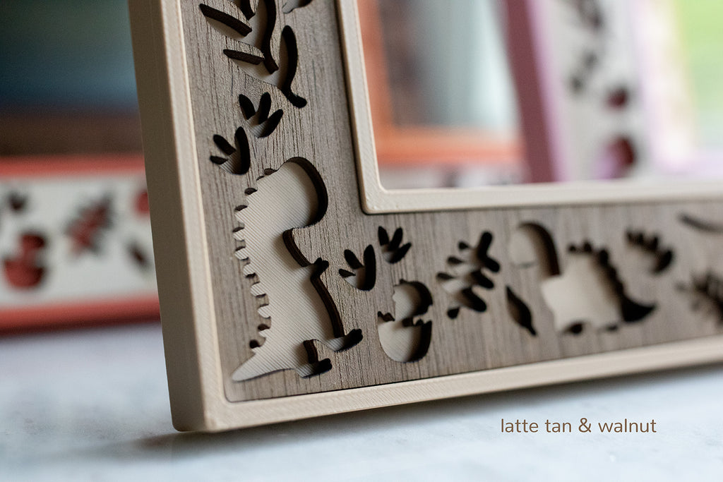 Close-up detail view of a laser cut dinosaur and dinosaur tracks in the corner of a personalized dinosaur themed picture frame. Includes a "latte tan" 3D printed housing and walnut inlay.