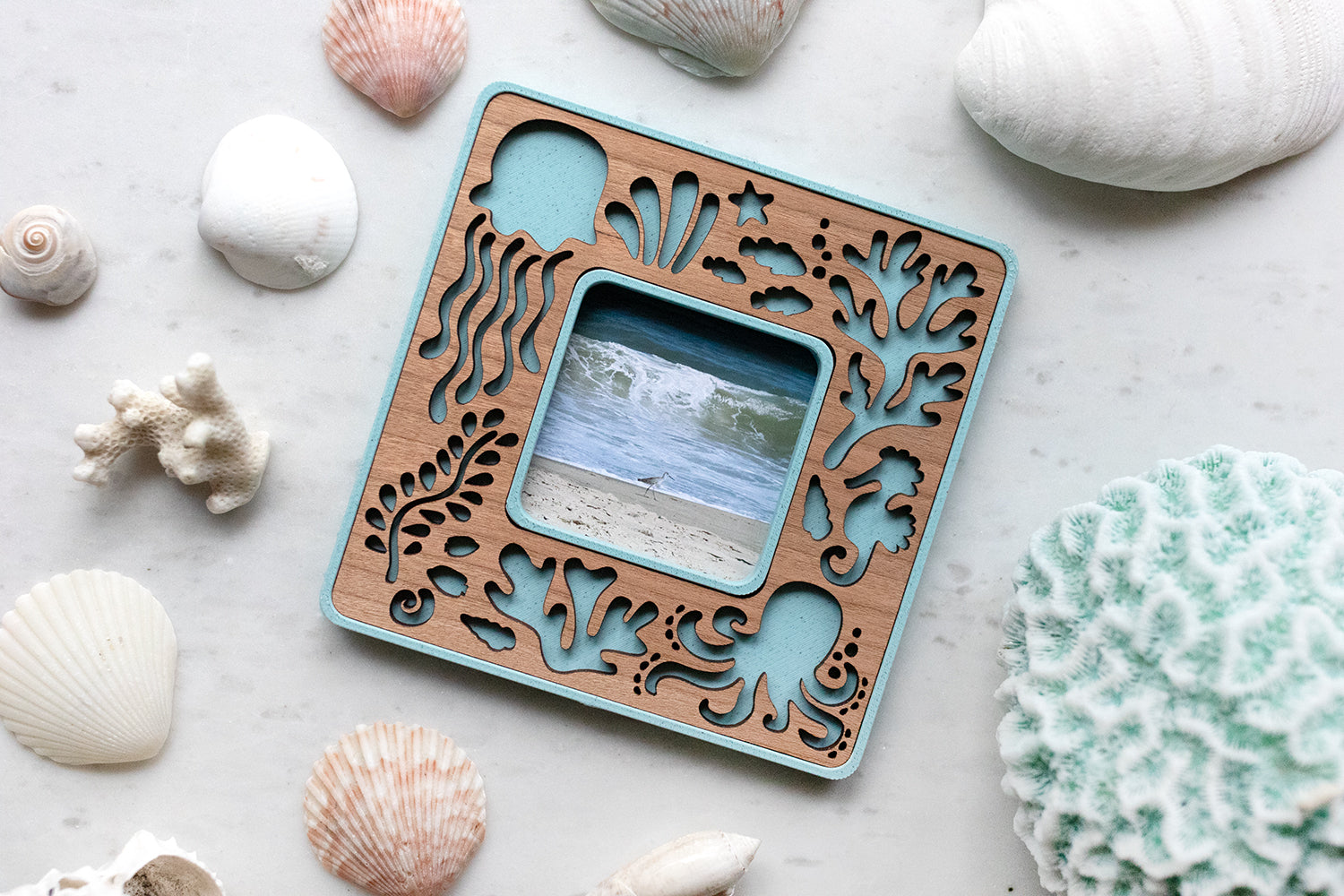 A tiny polaroid go frame with sea creatures design. Frame is light blue with laser cut cherry inlay. The frame is surrounded by seashells and displays a photo of the ocean and the beach. Customization options make a great small beach lover gift.