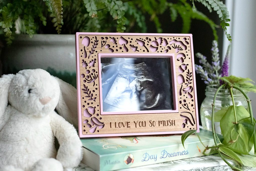 Camellia pink and cherry wood mushroom ultrasound frame engraved “I love you so mush,” with laser-cut woodland cutouts, holding a baby sonogram photo, a keepsake gift for baby showers and expecting moms.