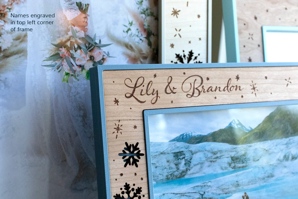 A close-up view of a newlywed couple's names engraved on a winter wedding picture frame. The engraving reads "Lily & Brandon" and features laser engraved snowflakes for a handcrafted winter wedding keepsake frame.