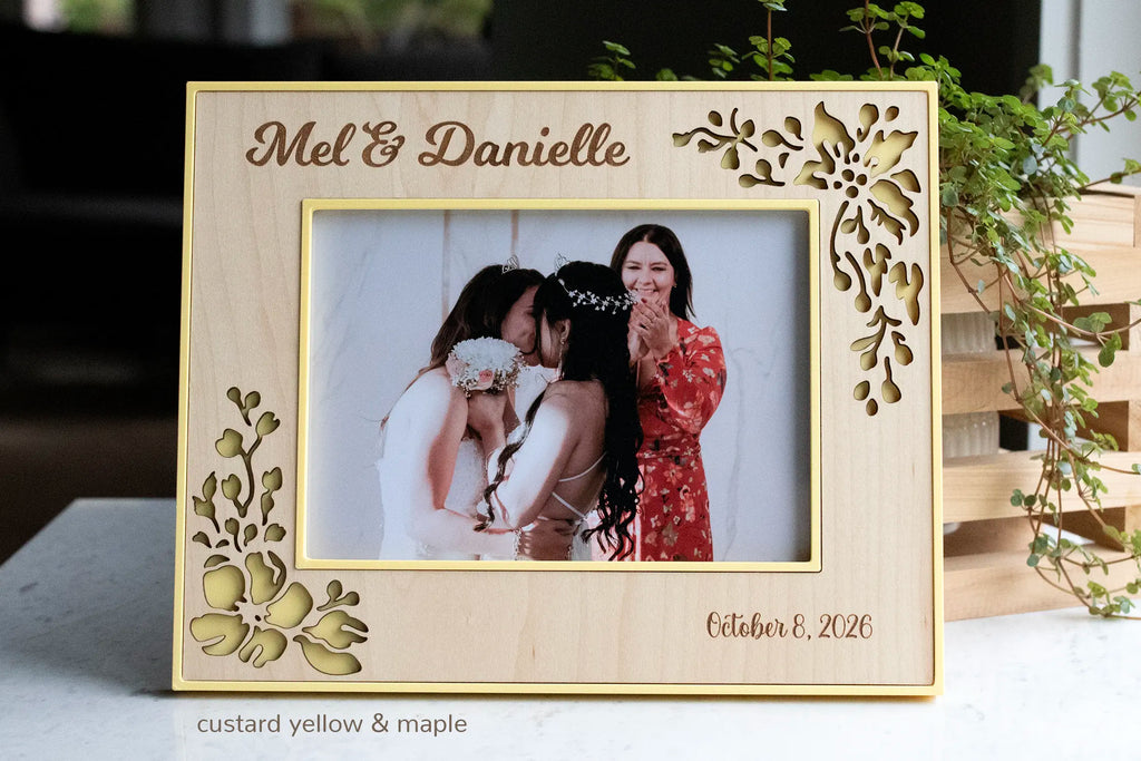 Personalized maple wedding frame with custard yellow housing, engraved couple’s names and wedding date, and laser-cut floral corners, holding a photo of two brides.