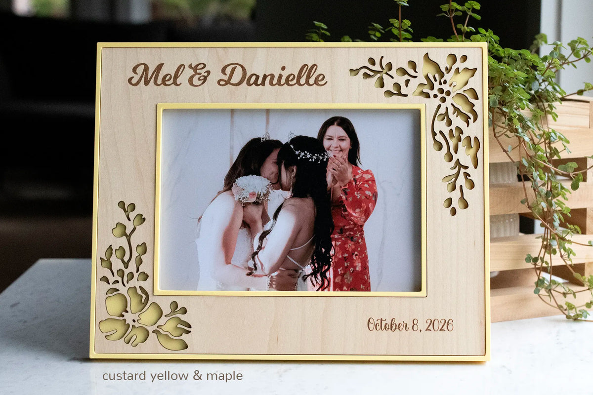 Personalized maple wedding frame with custard yellow housing, engraved couple’s names and wedding date, and laser-cut floral corners, holding a photo of two brides.